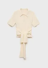 Jersey de punto fino color crema, con cuello polo, cierre frontal con botones, manga corta y diseño entallado con detalle de nudo en la cintura.