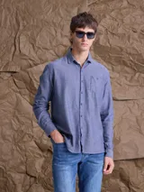 Camisa de manga larga en tono azul jaspeado, con cuello clásico, cierre frontal de botones y un bolsillo en el pecho.