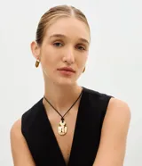 Conjunto de bijouterie compuesto por un collar con cordón encerado negro y dije de candado con llave en metal dorado texturizado, y aros colgantes a juego con forma de candado. El collar cuenta con cierre ajustable.