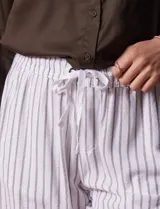 Short blanco con rayas verticales grises, de lino y rayón. Tiene pretina ancha elastizada con lazo de ajuste y bolsillos delanteros.