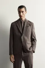 Blazer regular fit de Zara, confeccionada en tejido de lino y lana con diseño a cuadros en tonos marrones y grises. Cuenta con solapas de muesca, cierre frontal de un botón y bolsillos con solapa en la cadera.