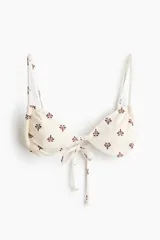 Top de bikini triangular color beige con estampado de pequeños motivos florales marrones y rosados, breteles ajustables y tiras para anudar en la espalda.