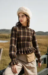 Blusa de manga larga con diseño cuadrillé en tonos marrones, beige y azul. Presenta cuerpo con fruncido tipo smock que ajusta la silueta, cuello alto con volado, mangas abullonadas con puños elásticos y volado en la cintura.