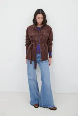 Chaqueta de gamuza en tono marrón oscuro, con cuello alto, cierre frontal con cremallera y botones a presión, bolsillos frontales con solapa y cinturón ajustable en la cintura.