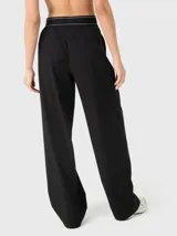 Pantalón de vestir negro de corte holgado y tiro medio, con cintura elástica estilo bóxer que presenta detalle de líneas blancas y logo bordado. Cuenta con pinzas delanteras y bolsillos laterales.