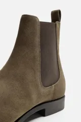 Bota estilo Chelsea de piel con acabado serraje color beige, con elásticos laterales para facilitar el calce, horma redonda y suela a tono con ligero tacón.