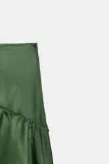 Falda midi de tiro medio color verde oscuro, confeccionada en tejido satinado con volantes en cascada y cierre lateral con cremallera oculta.