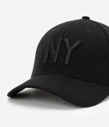 Gorra de seis paneles con ala curva, confeccionada en algodón color marrón. Presenta un bordado frontal con las letras NY en color blanco y cuenta con cierre strapback ajustable en la parte posterior.
