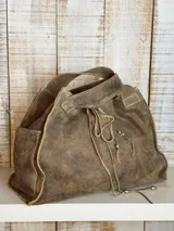 Bolso tipo shopper de cuero con acabado desgastado, color marrón. Presenta costuras visibles en contraste, bolsillo lateral externo y cierre mediante cordones ajustables con detalles metálicos.