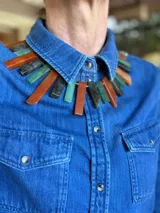 Collar corto elaborado con piedras rectangulares en tonos verdes, naranjas y grises oscuros, unidas con herrajes dorados y cadena de eslabones con dije colgante.