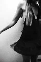 Vestido corto negro con escote en V profundo, estilo halter con tiras para atar al cuello. Presenta un diseño ajustado en el busto con tiras ajustables bajo el mismo que se cruzan y anudan en la espalda, y falda con volado en el ruedo con detalle de encaje.