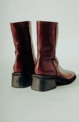 Bota de caña media confeccionada en cuero natural color bordó, con diseño minimalista, punta cuadrada y taco ancho de altura media.