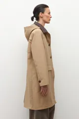 Trench impermeable color beige con cuello camisero en contraste de color marrón oscuro. Presenta cierre frontal con botones, bolsillos delanteros con solapa y mangas largas.