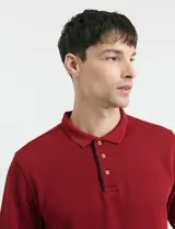 Remera de manga larga con cuello polo, confeccionada en tejido de punto canalé francés. Presenta abotonadura frontal con botones de madera y detalles a contratono en la cartera y el interior del cuello.