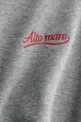 Buzo oversized de felpa color gris melange, con cuello redondo y hombros caídos. Cuenta con un pequeño bordado rojo con texto en el pecho y puños y bajo con ribete acanalado.