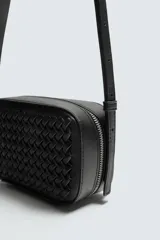 Bandolera pequeña de color negro con cuerpo rectangular y textura trenzada en el frente. Posee un asa de hombro ajustable y extraíble.