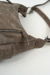 Bolso de hombro color marrón con acabado efecto cuero desgastado. Presenta dos bolsillos frontales verticales con cierre metálico, compartimentos laterales abiertos y una correa larga ajustable y extraíble.