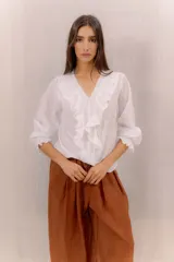 Camisa blanca de algodón con escote en V, volados delanteros con detalles de encaje y mangas largas con puños fruncidos.
