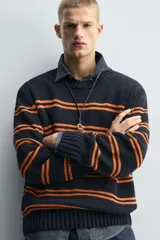 Jersey de punto con ajuste relajado, cuello redondo y manga larga. Presenta un diseño de rayas horizontales en color naranja sobre una base de color azul marino, con acabados en rib en puños, cuello y ruedo.