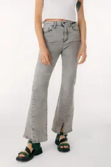 Jean azul claro de corte flare con aberturas en los tobillos y detalles rotos en las rodillas y muslos.