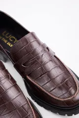 Mocasines negros de estilo clásico con textura de cuero grabado tipo cocodrilo. Presentan una banda frontal característica y suela plana con borde definido.