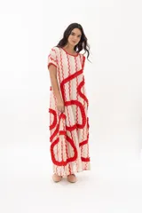 Vestido largo tipo remerón con estampado a rayas verticales en tonos beige, rosa y rojo. Presenta escote redondo y volados rojos en forma de espiral.