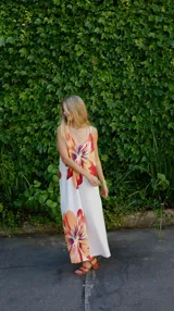 Vestido largo tipo solera con estampado floral de hibiscos en tonos naranjas y rojos sobre fondo blanco, con breteles finos y escote en V.