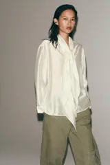 Camisa de tejido satinado con mezcla de lyocell, cuello redondo con escote en pico y lazada frontal. Presenta mangas largas con puños anchos y bajo recto.