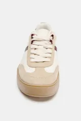 Zapatilla tipo bamba con diseño de paneles en combinación de colores y materiales, incluyendo detalles en cuero sintético y gamuza. Presenta suela de plataforma en contraste y cierre mediante cordones.