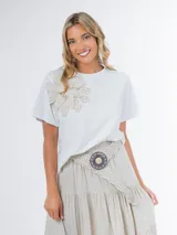 Remera blanca de tejido liviano con aplique de flor de crochet en el frente.