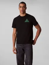 Remera de algodón negro con cuello redondo y mangas cortas. Presenta un diseño gráfico geométrico en forma de pirámide compuesto por las siglas CK en color verde en el pecho.