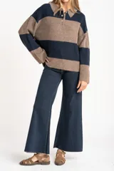 Sweater de tejido de punto color blanco roto o crema, con textura jaspeada. Presenta cuello polo y un escote con tres botones nacarados. El calce es holgado (oversize) y tiene mangas largas.