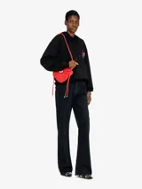 Bolso bandolera Diesel modelo Scrunch-D Heart, de color rojo y diseño en forma de corazón. Confeccionado en piel con acabado brillante y arrugado, presenta el logotipo D de metal con cristales en el centro, cierre de cremallera doble y correa ajustable.
