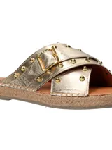 Sandalias tipo ojota con tiras cruzadas en cuero metalizado dorado, decoradas con tachas metálicas y hebilla lateral. Presentan una base con detalle de yute trenzado alrededor del contorno.