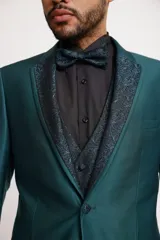 Traje de tres piezas color bronce con acabado satinado, compuesto por saco entallado, pantalón de vestir y chaleco con solapas estampadas en tonos grisáceos. Incluye moño a juego.