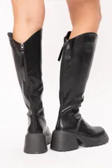 Bucaneras de caña alta con diseño curvo en la parte superior, confeccionadas en material sintético negro con acabado brillante. Presentan una suela track con plataforma y taco cuadrado robusto, además de cierre lateral.