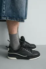 Zapatilla deportiva de estilo urbano con cordones, confeccionada en una combinación de piezas de cuero sintético. Presenta un diseño con detalles en contraste, suela con volumen bicolor y tirador en el talón.