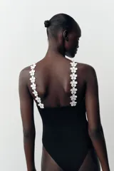 Body negro de tejido elástico con escote halter y detalle de flores blancas aplicadas en el contorno.