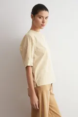 Camisa de manga corta color beige con sutiles rayas verticales blancas, cuello mao y cierre frontal oculto con botones.