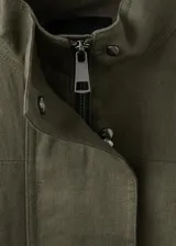 Chaqueta de lino color verde militar, diseño oversize con cuello alto, cierre oculto, manga larga con puño abotonado y cinturón ajustable en la cintura.