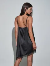 Vestido midi negro de satén con detalles de encaje en el escote, el ruedo y una aplicación diagonal que cruza el diseño. Cuenta con tirantes finos y un corte fluido.
