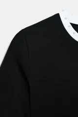 Camiseta blanca de manga corta y cuello redondo, con ribete negro decorado con perlas blancas en el cuello y los puños.