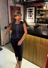 Chaleco tejido sin mangas, color negro, con textura brillante (lurex) y ribetes en azul. Presenta un escote redondo y se ata al frente con cordones.