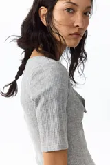 Top de manga corta de punto pointelle suave, color gris, con ajuste entallado, escote en U y hilera de botones frontales. Presenta ribete levemente festoneado en el escote y la tapeta.