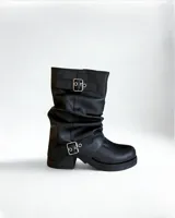 Bota negra de caña media, estilo motociclista, con efecto arrugado (slouchy) y hebillas decorativas en el empeine y en la caña. Posee suela de plataforma gruesa y taco bajo.