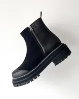 Botas cortas de cuero vacuno color negro, con diseño combinado de gamuza y cuero texturizado con efecto reptil en el talón. Presentan cierre lateral metálico, puntera reforzada y suela track dentada con costura visible.