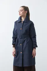 Trench de diseño clásico en color beige, con cierre frontal de botones, cinturón ajustable con hebilla a tono y mangas con trabillas en los puños.