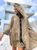 Vestido camisero de corte holgado y diseño escalonado, con estampado animal print en tonos beige y negro. Presenta cuello camisero, cierre frontal con botones y mangas largas con puños.