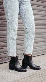 Bota tipo Chelsea de cuero negro, con paneles laterales elásticos y taco cuadrado de 6 cm con acabado de madera. Diseño clásico con puntera redondeada y tirador trasero.