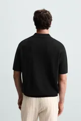 Polo de manga corta, color azul medio, tejido en punto perlado con cuello solapa y cierre frontal de cremallera.